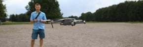 In foreground drone flies, guy controls drone 